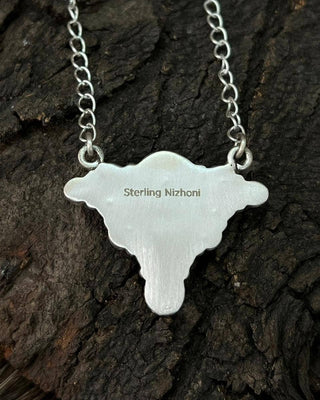A sterling silver custom name necklace shaped like a steer or longhorn cattle head, featuring the engraved name 'Sterling Nizhoni', displayed on a textured dark wood bark background.