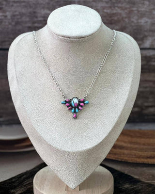 A silver chain necklace with a colorful beaded pendant displayed on a cream-colored jewelry bust against a rustic wooden background.