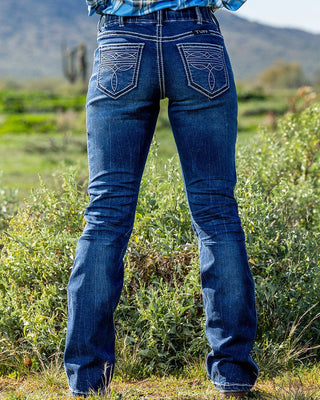 Person wearing blue jeans standing in a grassy field with mountains in the background