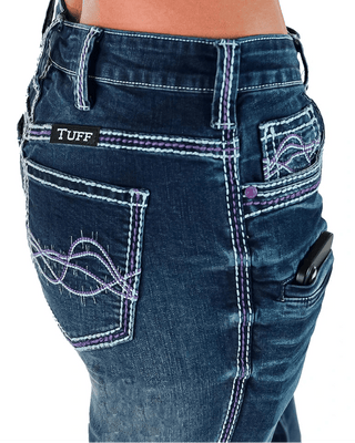 Close-up of the back waist and pockets of dark blue denim jeans worn by a model. The jeans feature purple and white contrast stitching, decorative embroidered stitching on the back pockets, a black TUFF brand patch on the left pocket, and a side pocket holding a black phone.