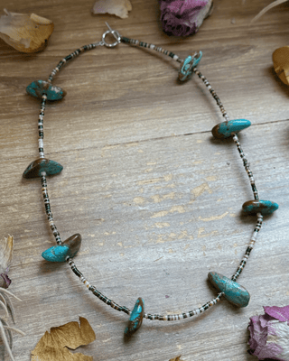 Necklace with turquoise stones on a wooden surface with dried leaves and flowers.
