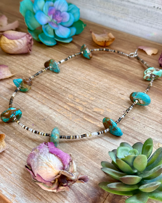 Necklace with turquoise beads on a wooden surface with flowers and succulents.
