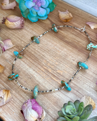 Necklace with turquoise stones on a wooden surface with dried flowers and plants.