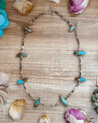 Necklace with turquoise beads on a wooden surface with flowers and plants