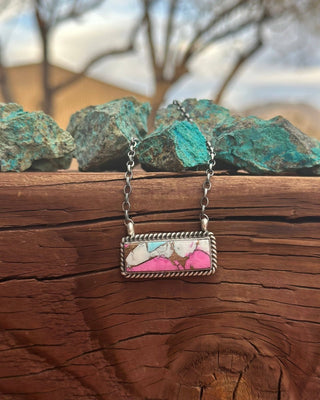 Necklace with a marbled pendant on a wooden surface with rocks and trees in the background