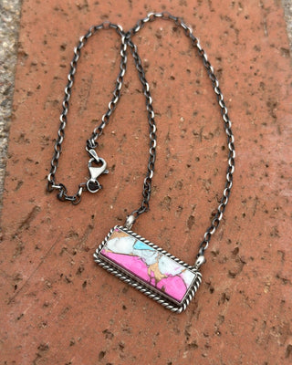 Necklace with a rectangular pendant featuring a pink and white design on a brick surface
