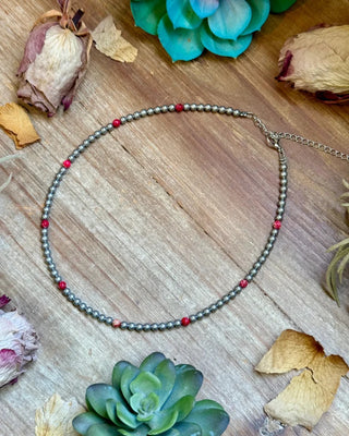 Necklace with red beads on a wooden surface with succulents and dried leaves.