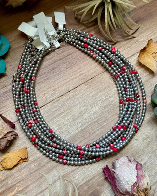 Necklace with red and silver beads on a wooden surface with dried leaves