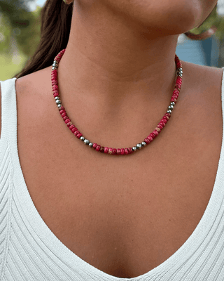 Person wearing a red and silver beaded necklace with a blurred outdoor background