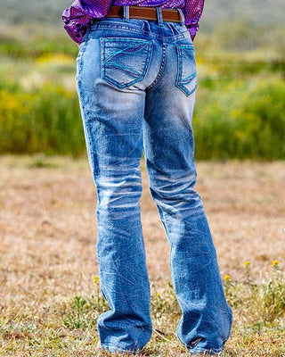 Woman in a purple shirt and cowboy hat standing in a desert landscape with mountains in the background.