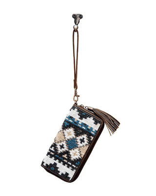 A zip-around wallet with a Southwestern geometric pattern in blue, beige, black, and white, featuring a brown leather wrist strap and tassel.