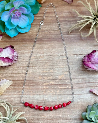 Necklace with red beads on a wooden surface with decorative plants and flowers.