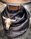 The Wynonna Wild Rag in Black tied around a wooden cable reel with a small cow skull on cowhide.