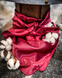 The Wynonna Wild Rag in Bula Burgundy tied around a wooden cable reel alongside cotton on stems.