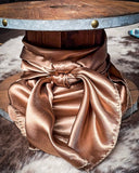 The Wynonna Wild Rag in Camel tied to a wooden cable reel, resting on cowhide.