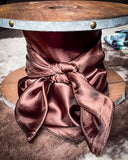 The Wynonna Wild Rag in Dark Coffe tied to a wooden cable reel resting on a backdrop of cowhide.