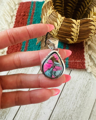 Colorful teardrop pendant held by a hand with pink nail polish on a wooden surface.