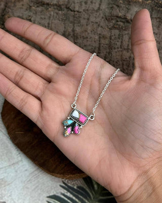 Necklace with colorful pendant held in a hand against a wooden background