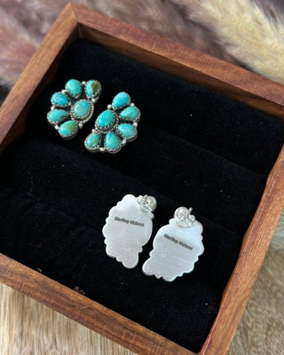 Turquoise earrings and silver leaf-shaped earrings in a wooden box with black interior.
