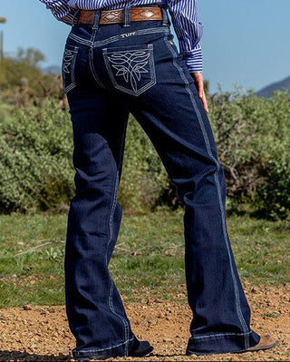 Person wearing a blue striped shirt, dark jeans, and a cowboy hat in a desert landscape.