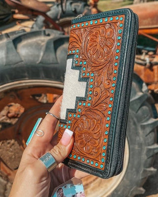Hand holding a leather wallet with intricate designs in front of a tractor.