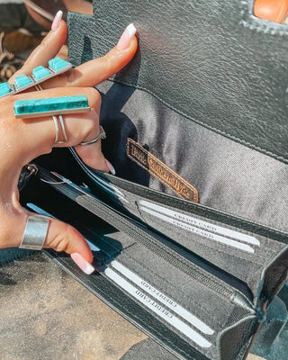Hand holding a black leather wallet with visible brand name, close-up shot.
