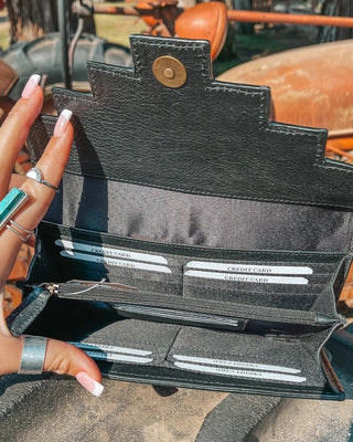 Person holding a black wallet with visible card slots against a rustic background