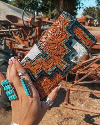 Hand holding a decorative wallet with intricate patterns and turquoise accents, set against a rustic background.