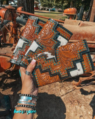 Handmade leather goods with intricate designs held by a person outdoors.