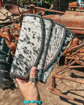 Hand holding three black and white hide wallets against a rustic background.