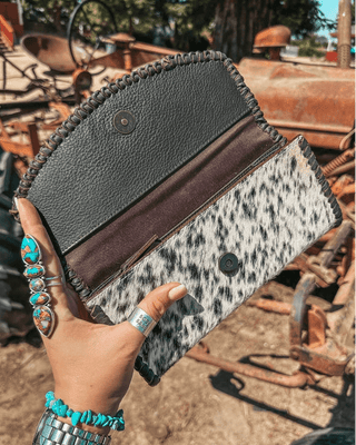 Hand holding a black and white hide wallet against a rustic background.
