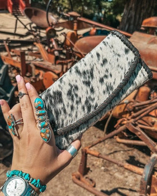Hand holding a cowhide wallet with turquoise jewelry against a rustic background