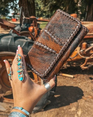 Hand holding a brown leather wallet with a rustic background featuring an old tractor.