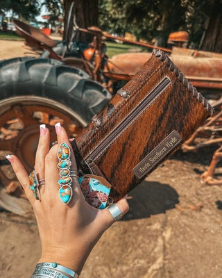 Hand holding a wallet with jewelry in front of a rustic background