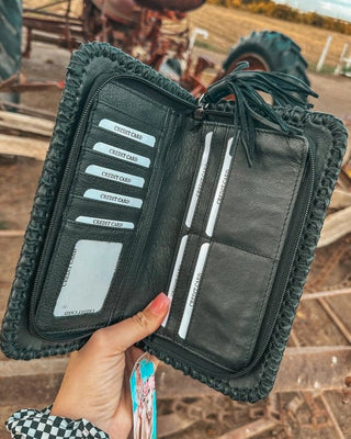 Black wallet with card slots held by a hand against a rural background with tractors.