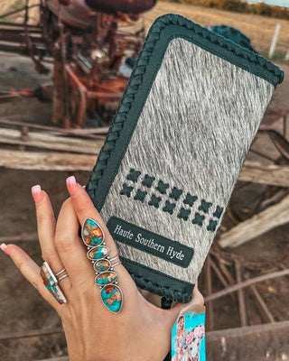 Hand holding a wallet with 'Hauté Southern Hyde' branding in an outdoor setting.