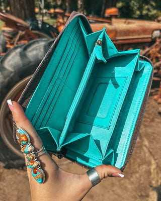 Teal wallet held by a hand with a scenic background