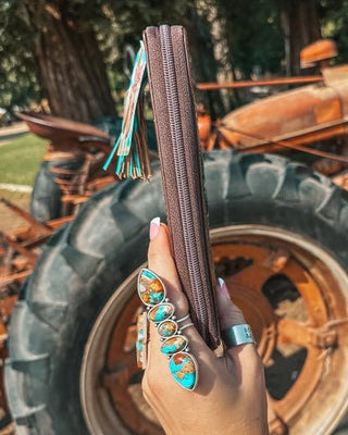 Hand holding a wallet in front of a rustic background with large wheels and rusty machinery.