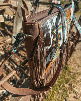 Close-up of a leather bag with intricate patterns and fringes, set against a natural outdoor background.