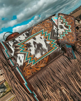 Close-up of a leather bag with intricate patterns and fringes against a cloudy sky.