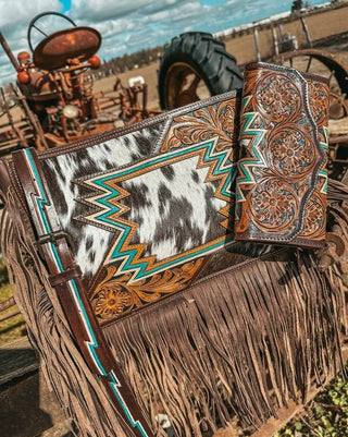 Cowhide leather clutch with intricate patterns and fringes on a rustic background