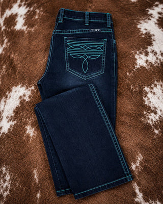 A pair of dark blue denim jeans laid flat on a brown and white cowhide rug. The back pocket features a large turquoise embroidered graphic, and the brand name 'TUFF' is visible on the waistband.