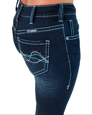 Close-up of a person wearing dark blue denim jeans, showing the back pocket with decorative white and light blue stitching and a visible TUFF brand patch.