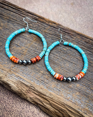 Turquoise hoop earrings with small orange and black beads, displayed on a rustic piece of wood.