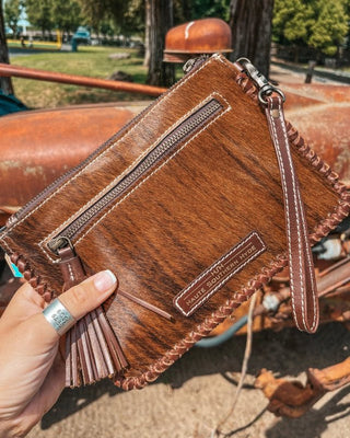 Brown leather clutch held by a hand with a blurred outdoor background