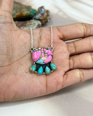 Colorful necklace with an oval-shaped pendant held in a hand against a neutral background