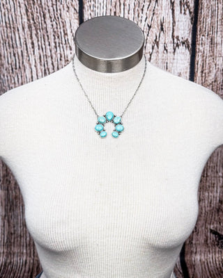 Turquoise colored squash blossom necklace displayed on mannequin bust with rustic wood background.