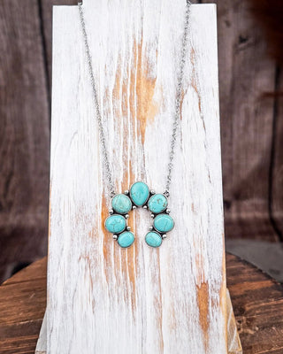 Rustic turquoise colored squash blossom necklace on distressed white wooden display board.