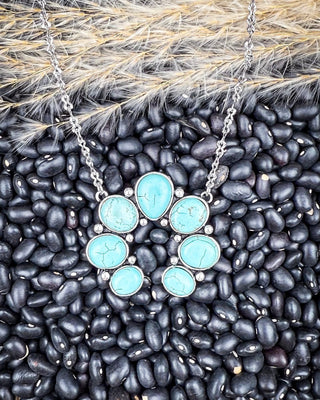 Faux turquoise squash blossom necklace on black beans and wheatgrass background.