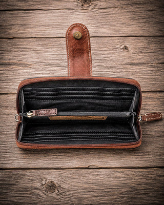 An open brown leather zip-around wallet with multiple card slots and an interior coin pocket, displayed on a rustic wooden plank background.